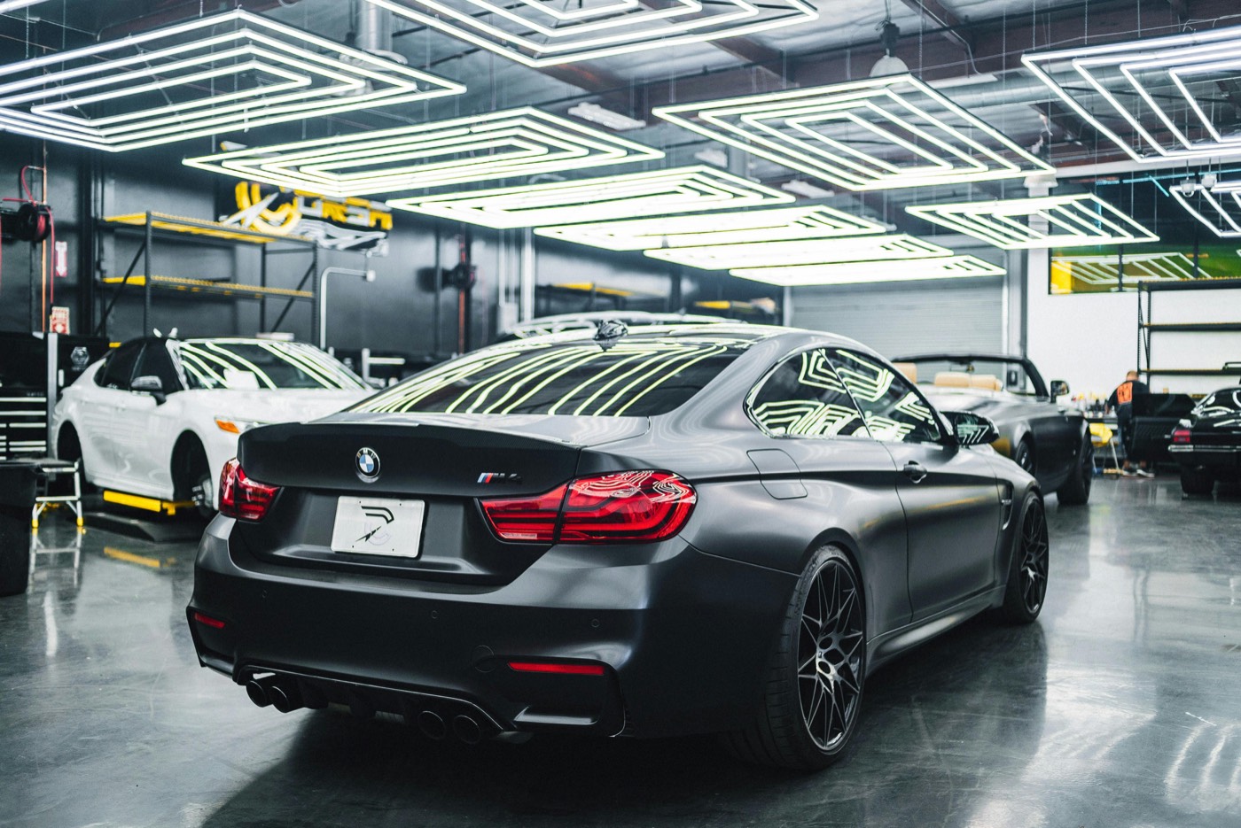 Matte-black BMW M4 in a modern car dealer showroom under geometric ceiling lights